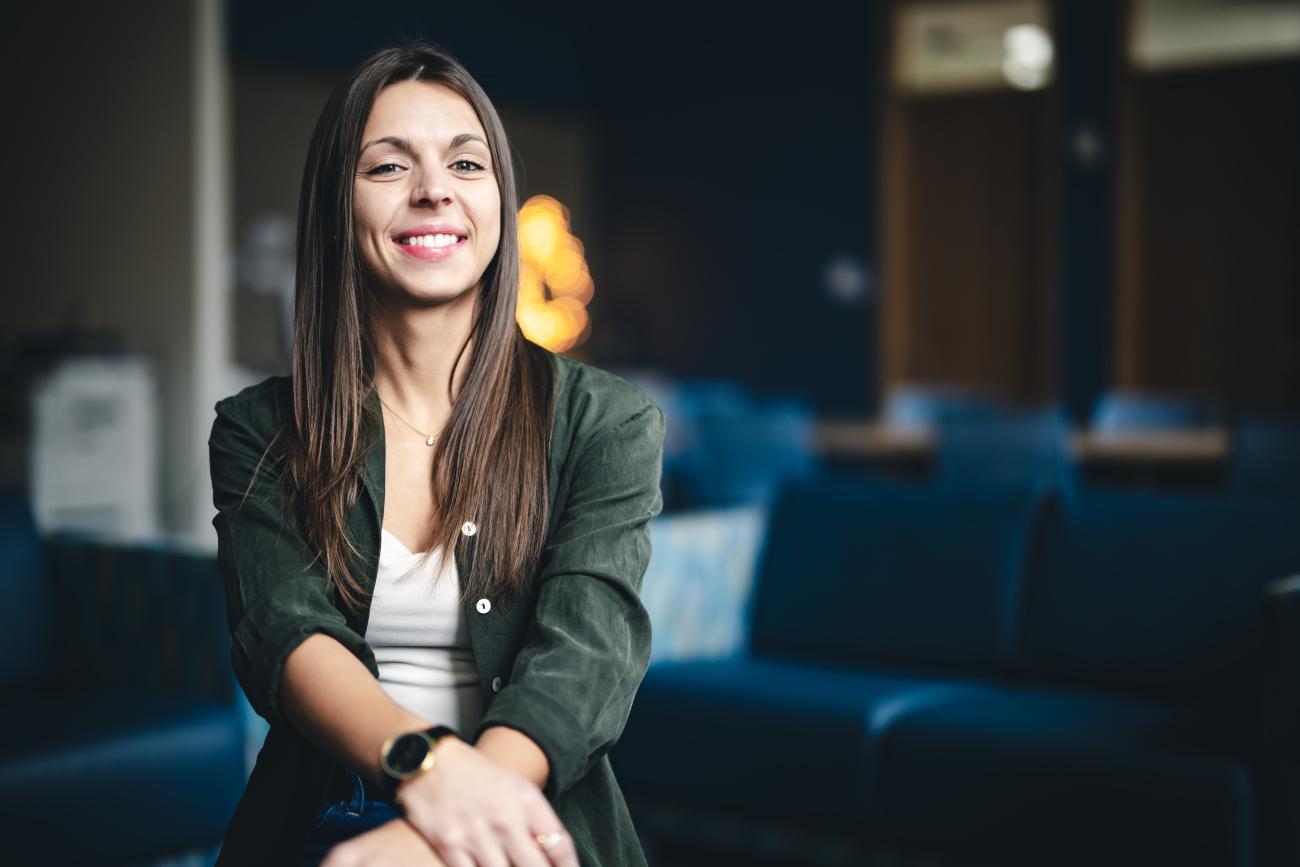 Haley Bennett sits on sofa and smiles at the camera for a portrait.